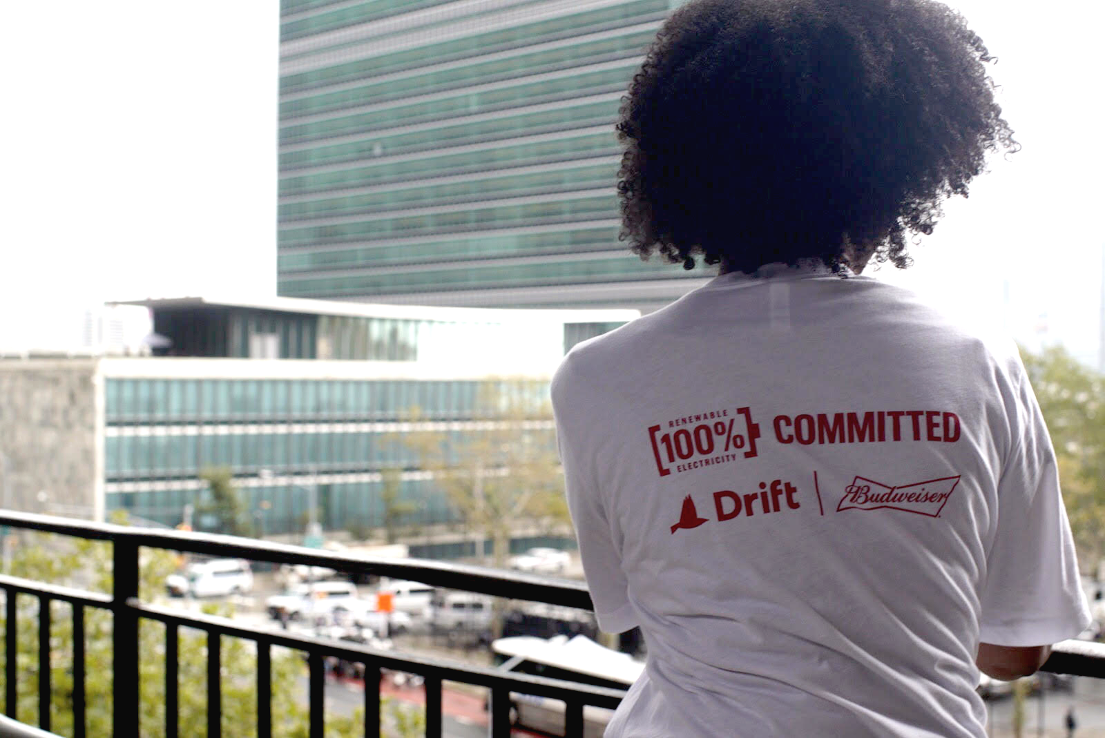 Woman wearing Drift and Budweiser t-shirt looks out at buildings from a balcony